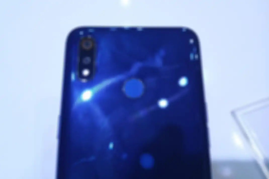 Ilustrasi bagian belakang Realme 3 lebih dekat. Tampak pada gambar ada dua kamera yang masing-masing memiliki sensor 13 megapiksel dan 2 megapiksel dilengkapi dengan LED flash. Pinggiran kamera utama diwarnai aksen bulatan ikonik Realme berwarna oranye. Ada pula pemindai sidik jari di punggung ponse