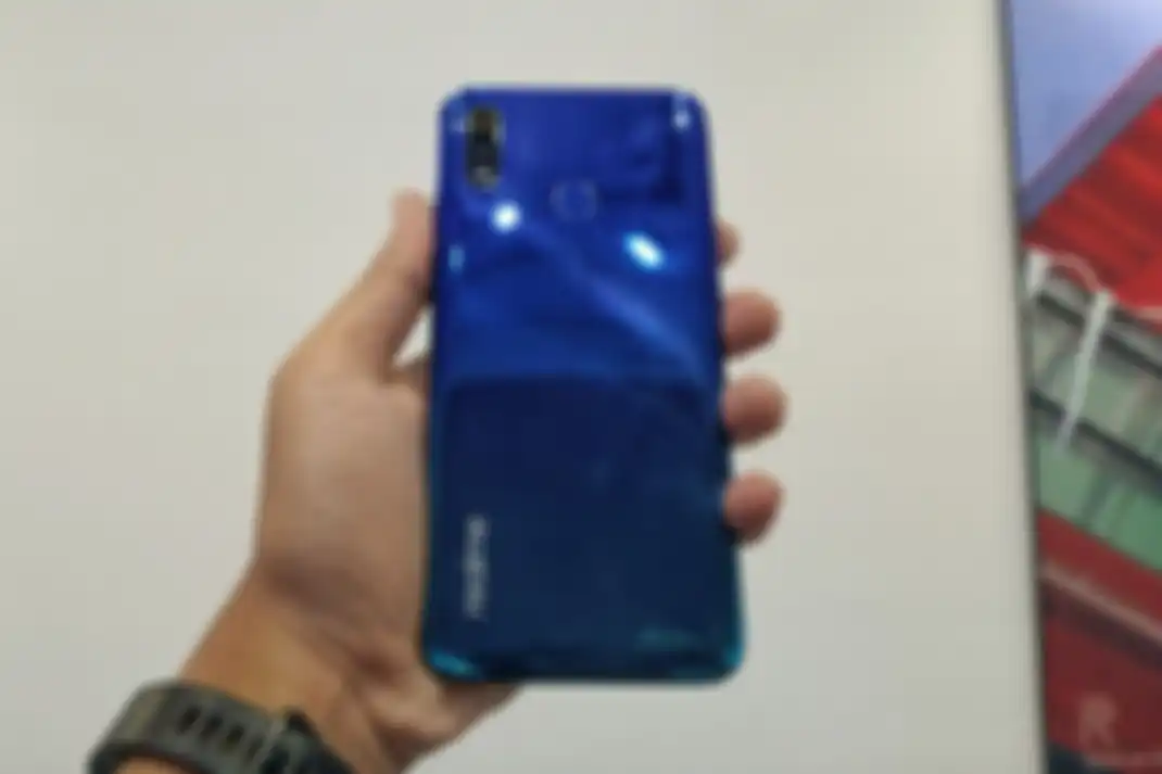 Ilustrasi bagian belakang Realme 3 dalam genggaman. Tampak ada dua buah kamera, LED flash, pemindai sidik jari, serta tulisan. 