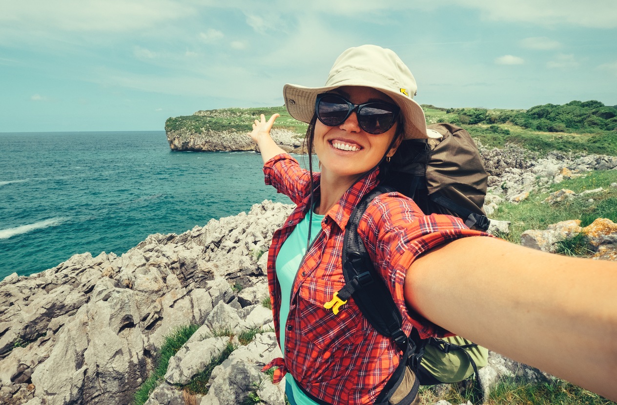Happy woman backpacker traveler take a selfie photo on amazing ocean coast