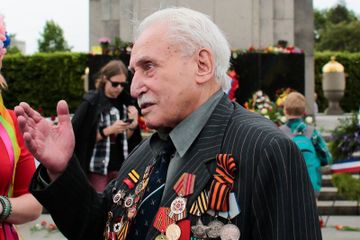 Veteran perang Soviet David Dushman, 92, tengah, berbicara kepada orang-orang yang memegang bendera Ukraina saat ia menghadiri upacara peletakan karangan bunga di Russian War Memorial di distrik Tiergarten di Berlin, Jerman. Dushman, prajurit Sekutu terakhir yang masih hidup yang terlibat. (Markus Schreiber)