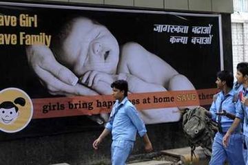 Pelajar di India berjalan melewati papan reklame di New Delhi yang mengkampanyekan perlindungan bayi perempuan.