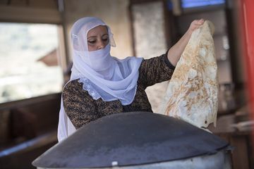 Seorang wanita Druze dengan pakaian tradisional sedang memanggang pitta, roti pipih khas daerah tersebut.