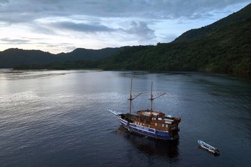 Salah satu kapal ekspedisi yang digunakan oleh tim peneliti dengan latar pegunungan di Pulau Nila, Kabupaten Maluku Tengah, Provinsi Maluku. 