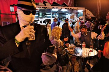 Para tamu pesta Halloween menikmati makanan segar dari truk-truk jajanan dalam pesta dansa berkostum.
