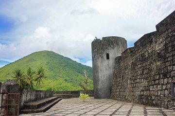 Benteng Belgica dengan latar Gunung Api. Benteng ini dibangun untuk melindungi perdagangan pala VOC dari serangan pemberontak lokal, setelah direbut dari Portugis. VOC sering mendirikan dan merebut benteng pada abad ke-17 dan 18 sebagai upaya monopoli perdagangan.