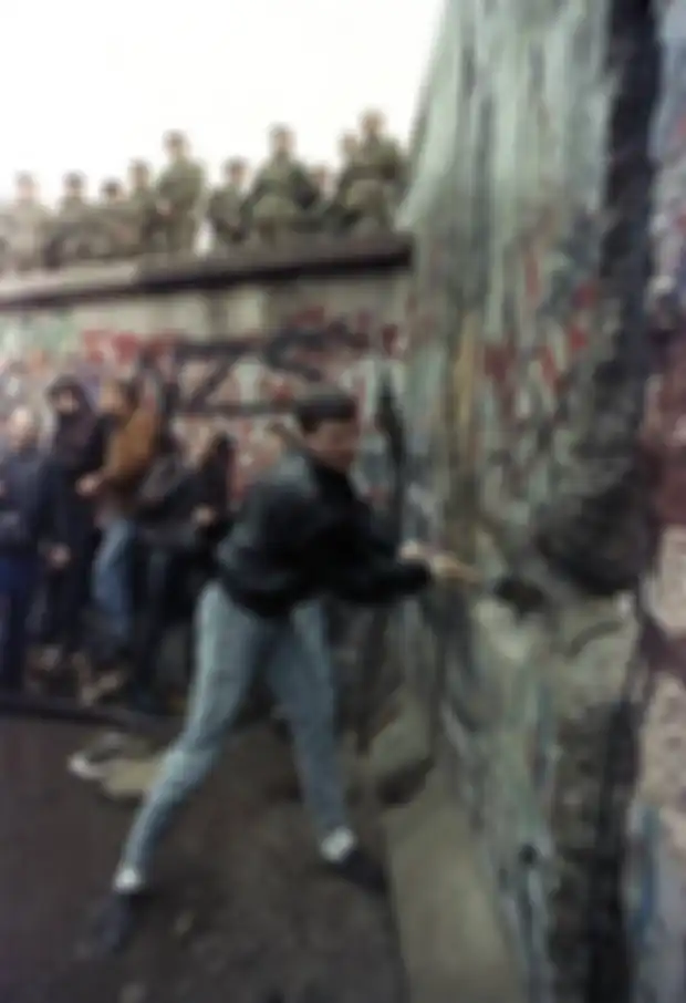Seorang demonstran memukul Tembok Berlin ketika penjaga di perbatasan Berlin Timur melihat dari Gerbang Brandeburg pada 11 November 1989