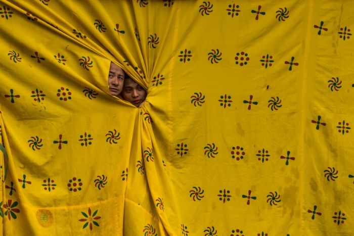 Dari balik tirai berwarna kuning moster, dua biksu mengintip para penari yang tengah tampil dalam perayaan Thimpu Tshechu di Bhutan.