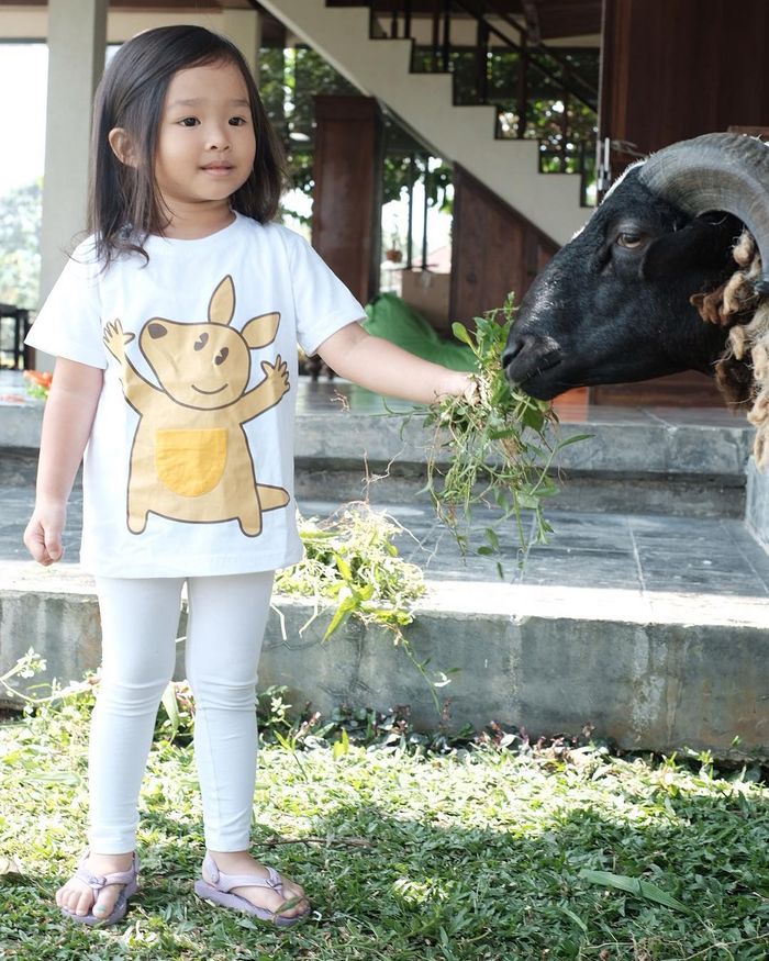 Thalia terlihat santai memberi makan seekor kambing.