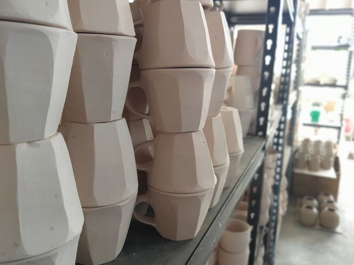 Ratusan cangkir dan piring dengan berbagai macam bentuk yang belum dihias tersusun rapi di rak.