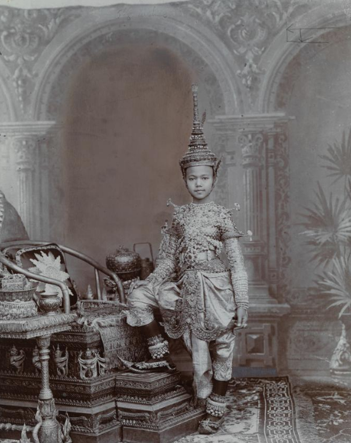 Seorang Pangeran Siam mengenakan pakaian penuh permata dan topi baja yang mengikuti model chadok, hiasan kepala yang biasa dikenakan penari tradisional Thailand.