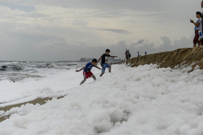 Anak-anak bermain di tengah polusi busa di pantai Marina.