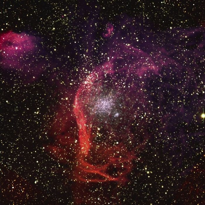 Gambar ini menunjukkan NGC1850, sekelompok ribuan bintang yang berjarak sekitar 160.000 tahun cahaya di Awan Magellan Besar, tetangga Bimasakti. Filamen kemerahan yang mengelilingi gugus, terbuat dari awan hidrogen yang luas, diyakini sebagai sisa-sisa ledakan supernova.