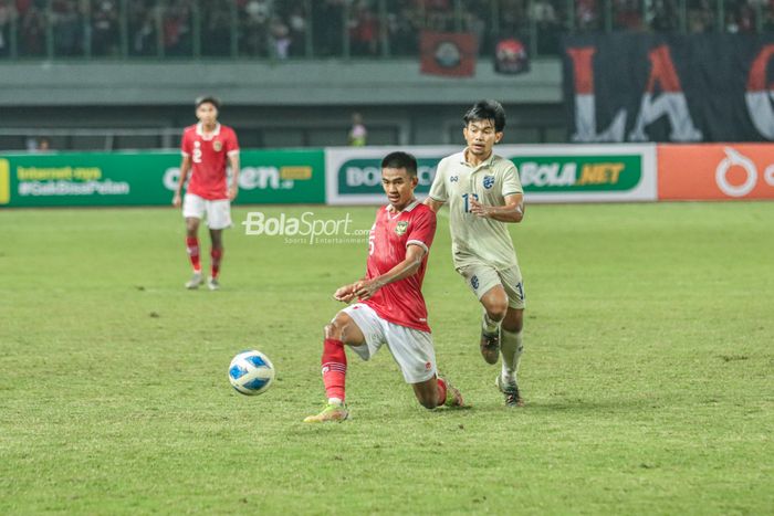 Bek timnas U-19 Indonesia, Kakang Rudianto (kiri), sedang mengoper bola dan dibayangi pemain timnas U-19 Thailand bernama Waris Chooithong (kanan) di Stadion Patriot Candrabhaga, Bekasi, Jawa Barat, 6 Juli 2022.