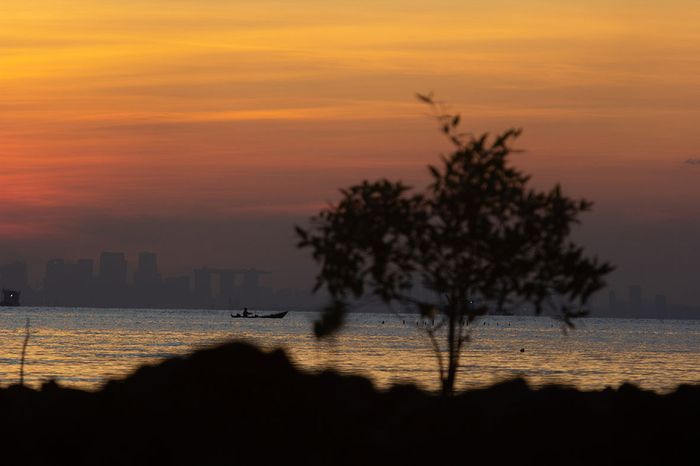 Kala matahari tenggelam, seorang nelayan Kampung Serip sedang memancing di dekat perbatasan Indonesia dengan Singapura yang berlatar belakang gedung pencakar langitnya.