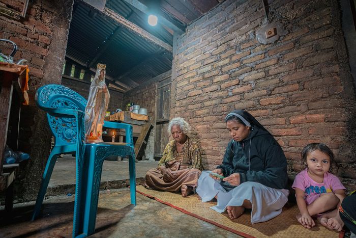 Di bawah cahaya lampu, Cornelia Rendut (kiri), seorang warga Desa Wewo, sedang mengikuti misa lansia. Setiap Minggu sore, suster dari paroki terdekat di Kabupaten Manggarai mengunjungi setiap rumah yang dihuni oleh lansia untuk pemberkatan hosti.