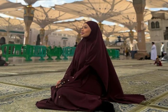 Rachel Vennya terlihat mengenakan pakaian berwarna coklat sambil duduk di Masjid Nabawi