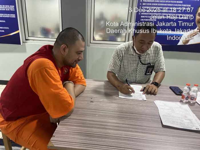 Ammar Zoni tengah duduk di hadapan sebuah meja dan tersenyum tanpa menghadap ke kamera