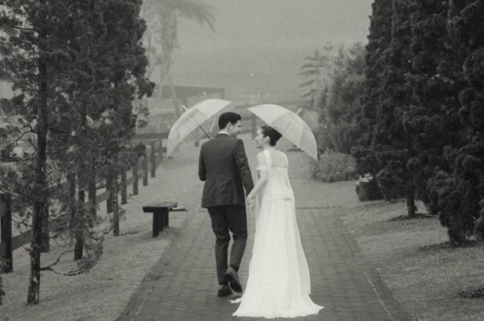Foto dari belakang kedua pasangan Ranty Maria dan Rayn Wijaya memperlihatkan mereka sedang berjalan beriringan sambil saling berpegangan payung