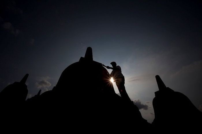 Seorang pria membersihkan Candi Borobudur dari lumut menggunakan sapu lidi kecil. Menurut pria terse