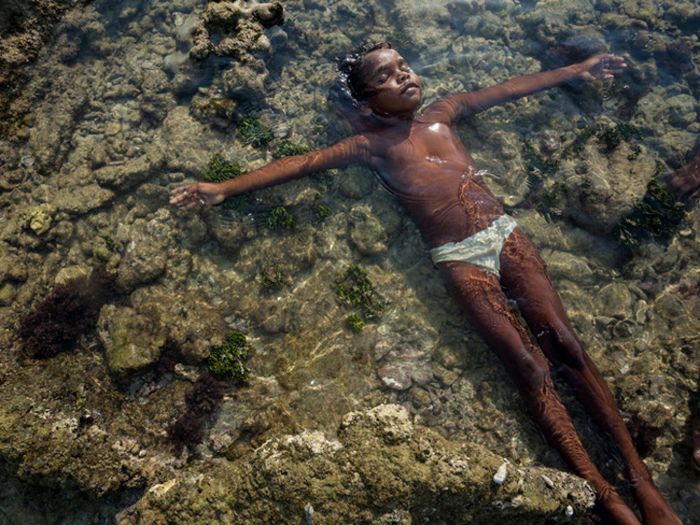 Anak perempuan Aborigin Yolngu menikmati hangatnya matahari dan lautan.