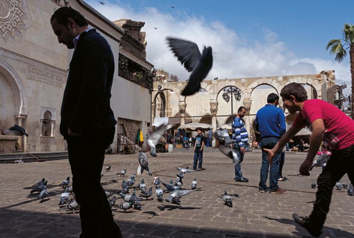 Di kawasan Kota Tua Damaskus, Suriah anak laki-laki iseng mengejar merpati yang berkerumun di alun-alun.