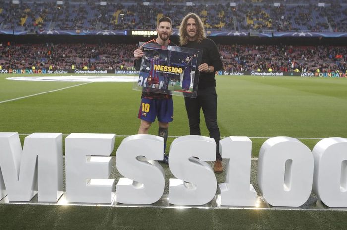 Kapten Barcelona, Lionel Messi, bersama mantan rekan sekaligus legenda El Barca, Carles Puyol, saat peringatan 100 gol Messi di ajang Liga Champions.