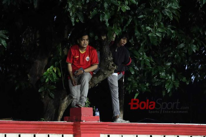 Suporter Persija Jakarta, The Jak Mania, terpaksa menaiki tembok dan pohon untuk menyaksikan pertandingan melawan Bhayangkara FC di Stadion PTIK, Melawai, Jakarta Selatan, Sabtu (14/3/2020)