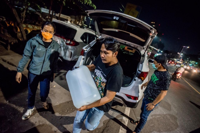 Ivo Ananda (kiri) dibantu tim Bonek Disaster Response Team untuk menurunkan cairan disinfektan. Ivo memberikan bantuan kepada BDRT sebanyak 250 liter cairan disinfektan. (Persebaya)