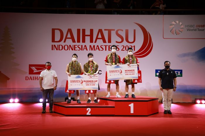 Marcus Fernaldi Gideon/Kevin Sanjaya Sukamuljo (jersey kuning) dan Takuro Hoki/Yugo Kobayashi berbaris di podium setelah final Indonesia Masters 2021 di Bali International Convention Centre, Nusa Dua, Bali, 21 November 2021.