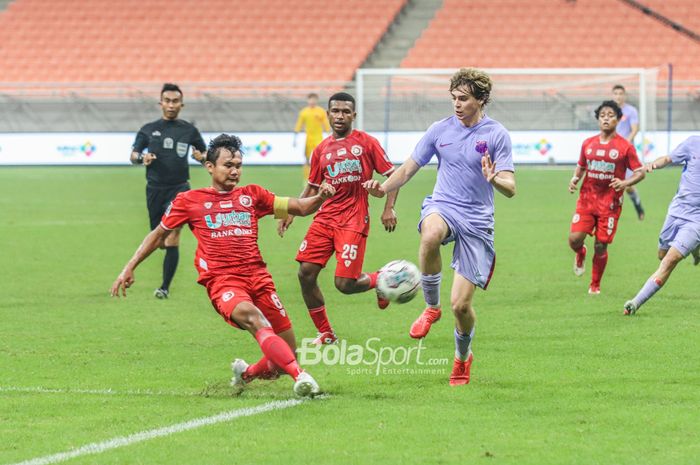 Bek Indonesia All Star, Komang Teguh Trisnanda (kiri), sedang menghalau bola yang dikuasai pemain Barcelona U-18, Cristobal Munoz Lopez (kanan), di Jakarta Internasional Stadium, Jakarta Utara, 13 April 2022.