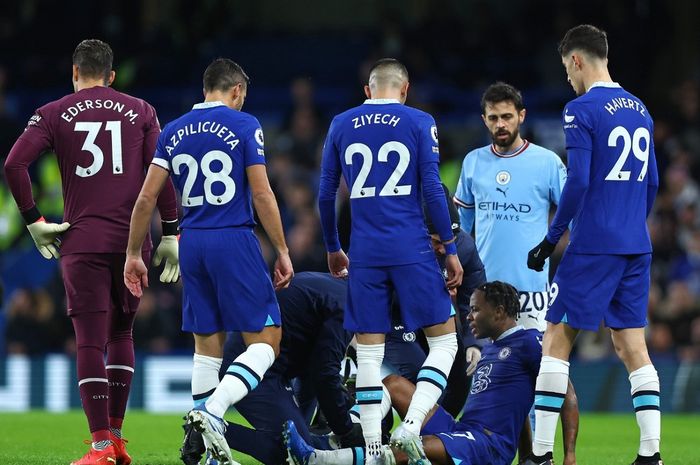 Winger Chelsea, Raheem Sterling (terduduk), saat mendapatkan perawatan dalam laga kontra Manchester City pada pekan ke-19 Liga Inggris 2022-2023 di Stamford Bridge, Kamis (5/1/2023).