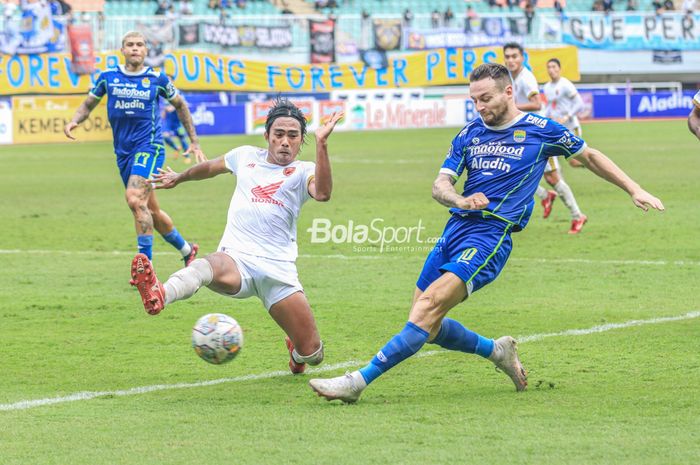 Gelandang Persib Bandung, Marc Klok (kanan), sedang mengoper bola dan berusaha dihalau bek PSM Makassar bernama Erwin Gutawa (kiri) dalam laga pekan ke-24 Liga 1 2022 di Stadion Pakansari, Bogor, Jawa Barat, Selasa (14/2/2023).