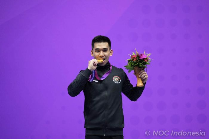 Atlet wushu Indonesia, Harris Horatius, menggigit medali emas Asian Games 2022 usai kuasai nomor Taolu Nanquan dan Nangun di Xiaoshan Guali Sports Centre, Hangzhou, China, Selasa (26/9/2023).