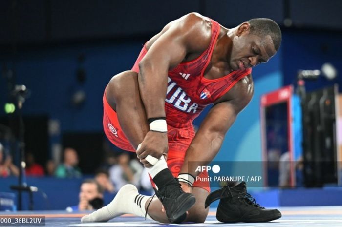 Atlet Kuba, Mijain Lopez, mencopot sepatu sebagai tanda pensiun setelah merebut medali emas Olimpiade ke-5 dari cabang gulat Greco-Roman nomor 120/130 kg, Selasa (6/8/2024) di Paris. 