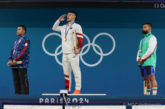 Lifter putra Indonesia, Rizki Juniansyah (tengah) saat upacara pemberian medali setelah meraih medali emas Olimpiade Paris 2024 di kelas 73 kg di South Arena, Paris, Jumat (9/8/2024) dini hari WIB.