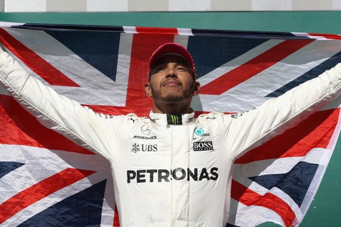 Juara GP Amerika Serikat, Lewis Hamilton (Mercedes), melakukan selebrasi dengan membentangkan bendera negaranya di atas podium kampiun di Circuit of The Americas, Austin, Texas, Minggu (22/10/2017).