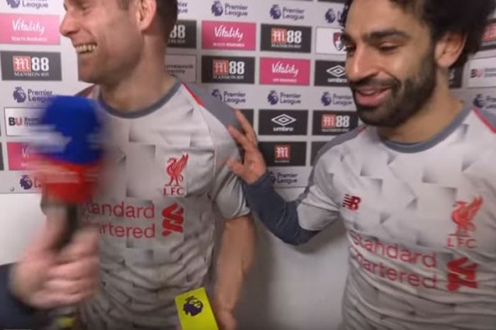 Usai mengalahkan Bournemouth 4-0, pada Sabtu (8/12/2018), winger Liverpool, Mohamed Salah, memberikan plakat gelar pemain terbaik pertandingan pada rekan setimnya, James Milner, di sesi wawancara. 