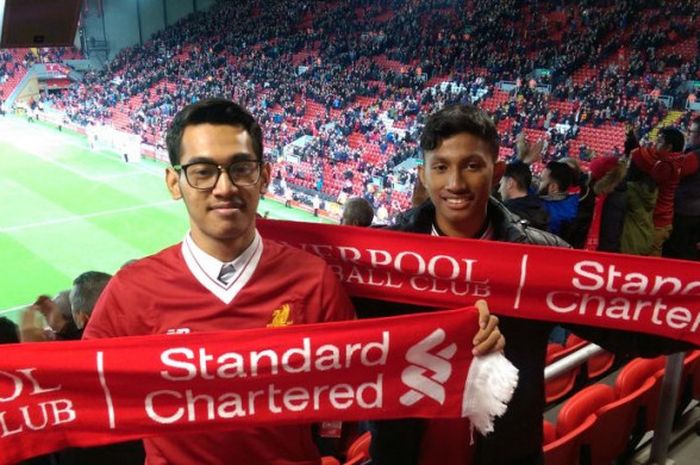 Pemenang Standard Chartered Cup 2017, Aditya Dimas (kiri) dan Rivaldo Lucas (kanan), berpose di depan Executive Suite Standard Chartered di Tribune Utama Stadion Anfield, dengan latar belakang lapangan dan tribune The Kop.