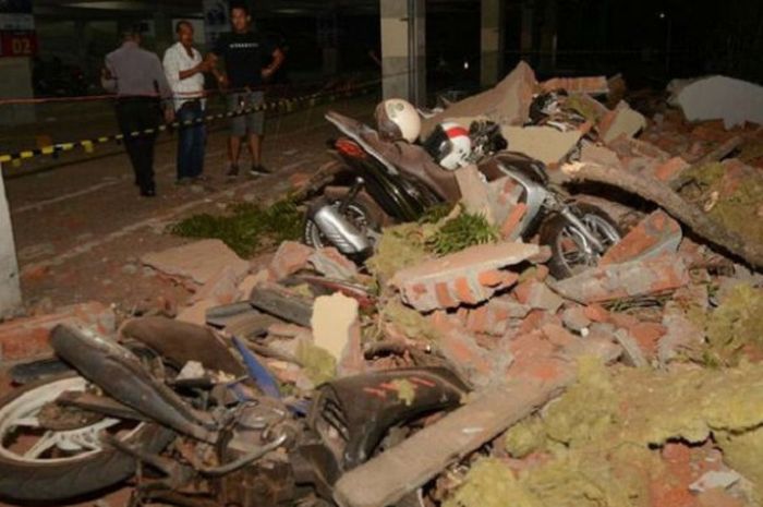 Warga melihat kendaraan yang hancur tertimpa puing bangunan yang runtuh akibat gempa, di salah satu mall, di Denpasar, Minggu (5/8/2018). Gempa yang mengguncang Lombok, Nusa Tenggara Barat, juga terasa hingga Bali.