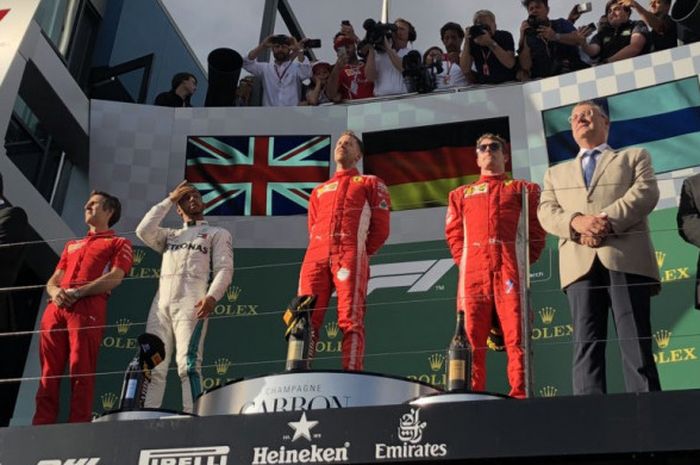 Pemenang balapan, Sebastian Vettel (Ferrari), menaiki podium bersama Lewis Hamilton (Mercedes) dan Kimi Raikkonen (Ferrari) usai balapan F1 GP Australia pada Minggu (25/3/2018).