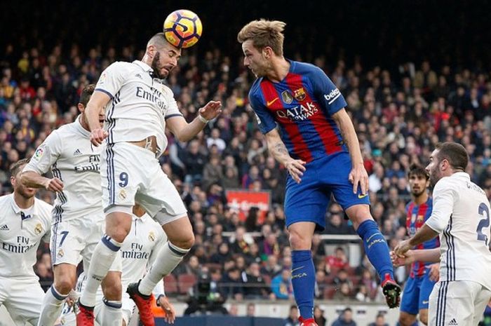 Striker Real Madrid, Karim Benzema (tengah kiri), menyundul bola di depan gawang Barcelona dibayangi gelandang Barcelona, Ivan Rakitic, dalam laga lanjutan Liga Spanyol 2016-2017 di Stadion Camp Nou, Barcelona, (3/12/2016).