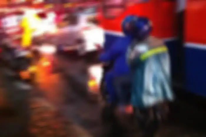 Pengendara sepeda motor yang menggunakan jas hujan ponco menutupi lampu rem dan sen.