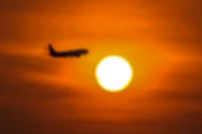 Boeing 737 sesaat akan mendarat dengan latar belakang matahari terbenam. 
