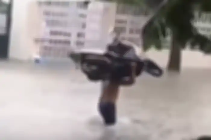 Seorang pria memanggul Yamaha Mio di tengah banjir