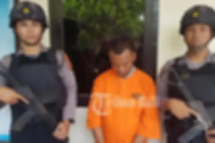 Suastika Saat berada di Mapolres Jembrana mengenakan rompi oranye dan borgol. 