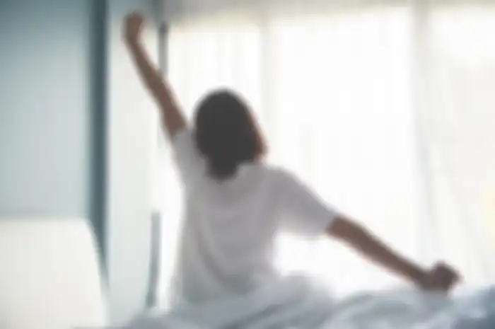 Asian woman waking up in the morning. Outstretched arms.