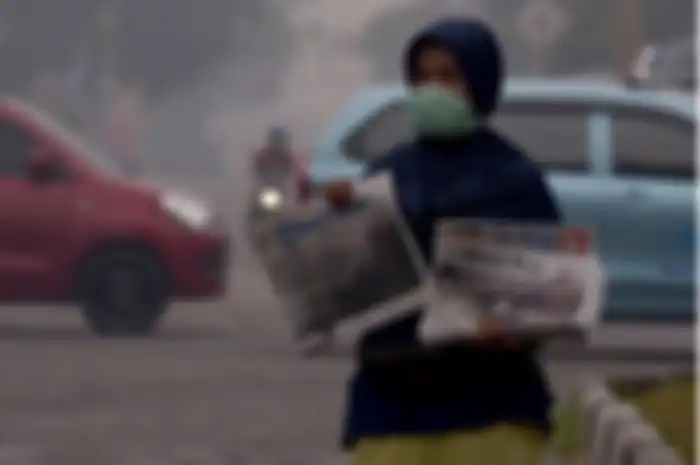 Seorang penjual koran mengenakan masker saat berjualan di tengah asap kebakaran hutan dan lahan (Karhutla) yang makin pekat menyelimuti Kota Pekanbaru, Riau, Jumat (13/9). 