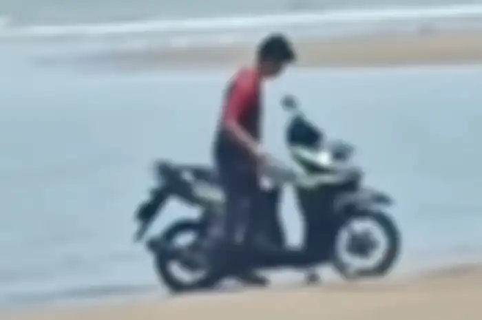 Seorang pria mencuci motor pakai air laut