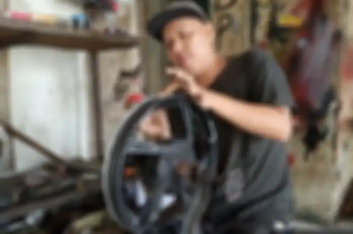Rudi Andali, pemilik bengkel Rudi Stel Velg Motor di daerah Cileungsi sedang memperbaiki pelek peang.