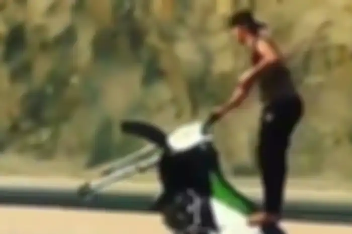 Seorang pria melakukan wheelie diatas motor tanpa roda depan.